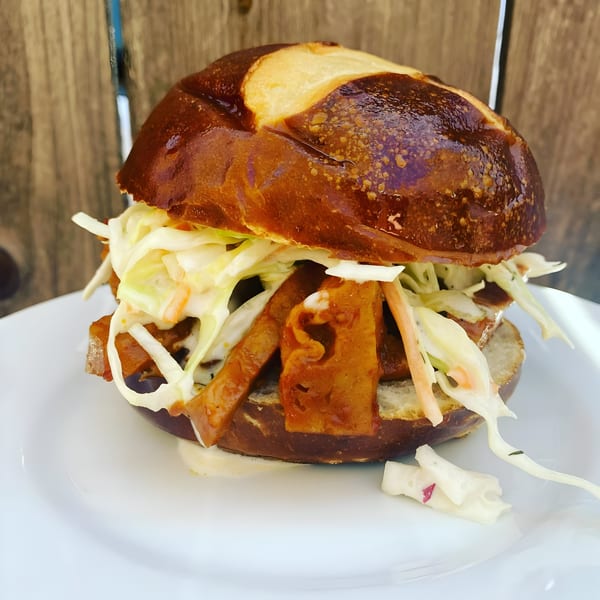 Vegan Daddy Meats' vegan sandwich with plant-based meat and coleslaw on a pretzel bun.