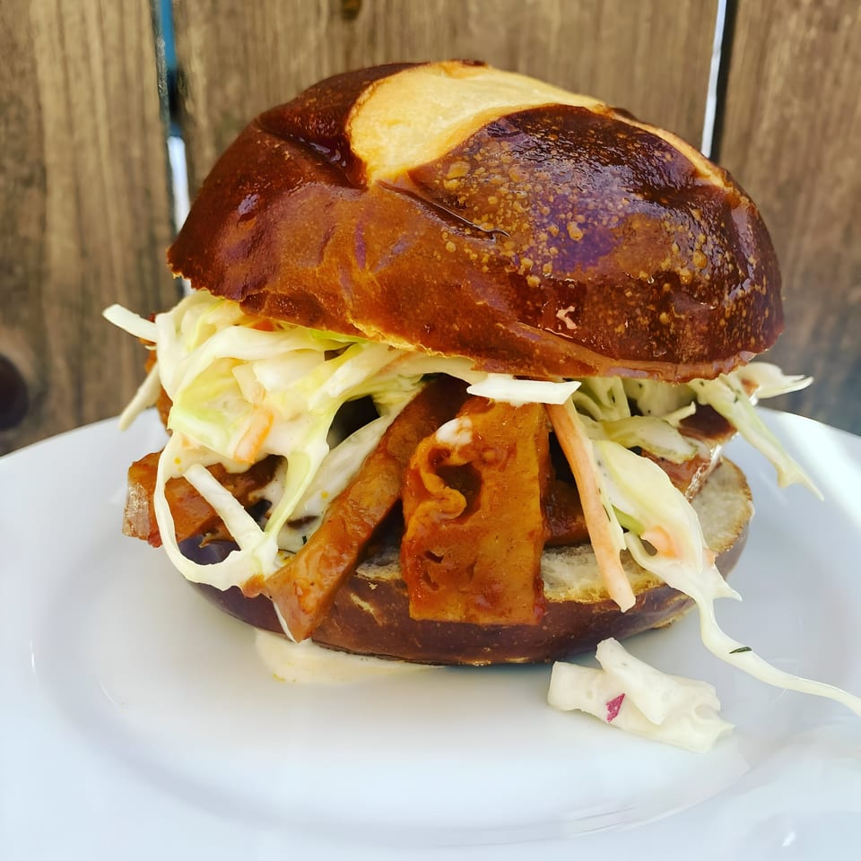 Vegan Daddy Meats' vegan sandwich with plant-based meat and coleslaw on a pretzel bun.
