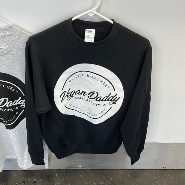 Black Vegan Daddy sweatshirt with a white circular logo, next to a gray sweatshirt.