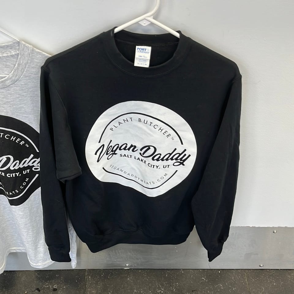 Black Vegan Daddy sweatshirt with a white circular logo, next to a gray sweatshirt.