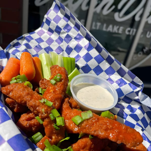 Vegan Daddy Meats' buffalo wings with carrots, celery, ranch, and green onions in a checkered basket.