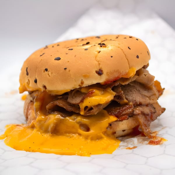 A vegan cheesesteak sandwich with melted cheese dripping onto white hexagonal paper.