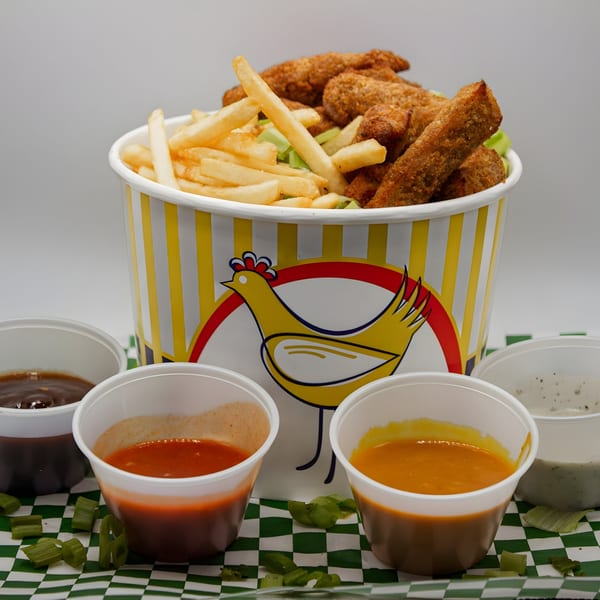 Vegan Daddy Meats' bucket of vegan chicken tenders and fries, with four dipping sauces.