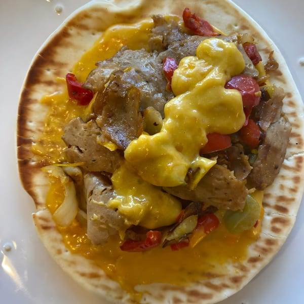 Vegan Daddy Meats' vegan cheesesteak on pita bread with plant-based meat, peppers, onions, and cheese sauce.
