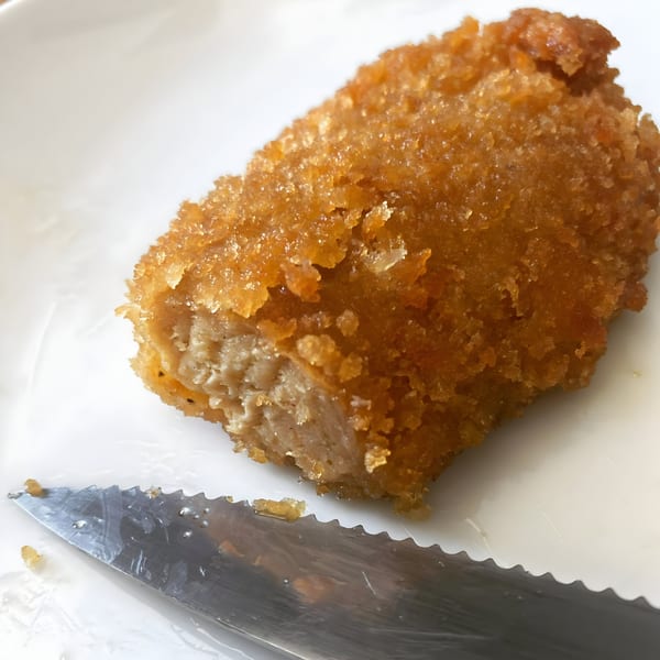A golden-brown vegan schnitzel, partially cut to reveal its meaty interior, on a white plate with a knife.